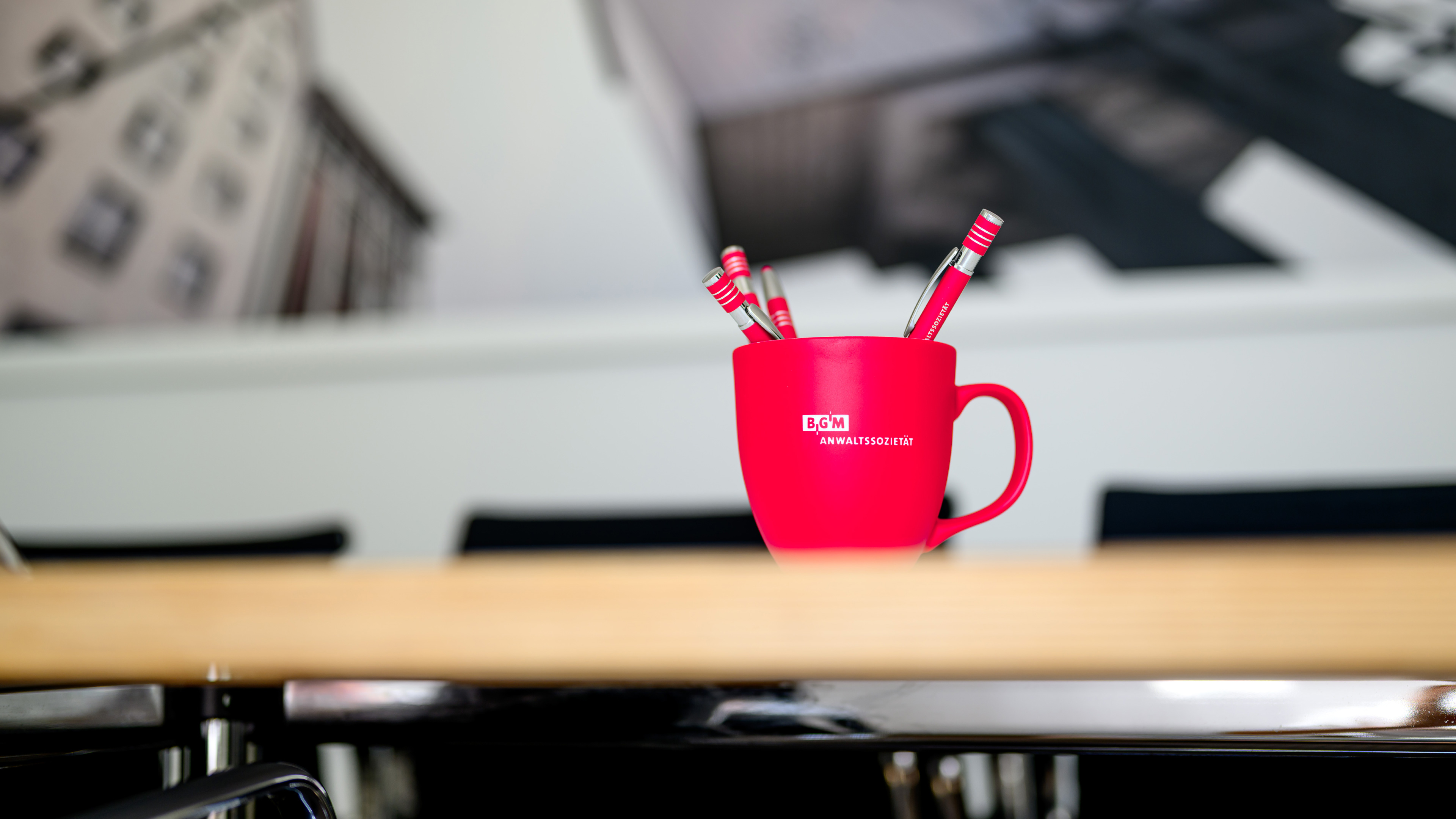 Eine rote BGM Tasse steht auf einem Tisch vor einem unscharfen Hintergrund